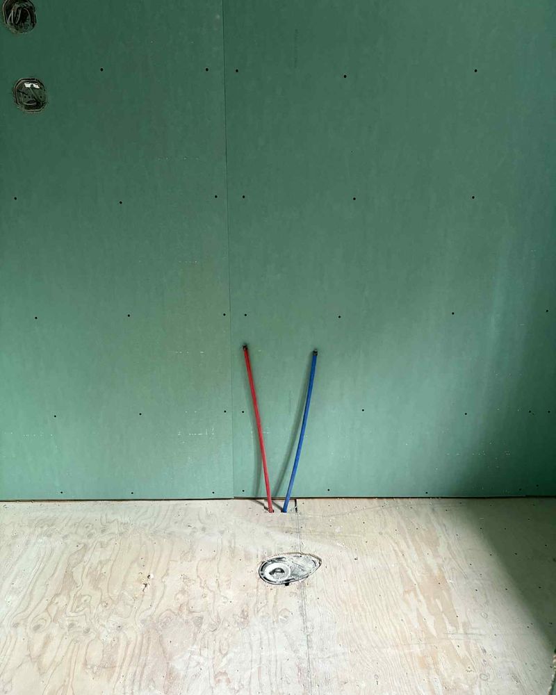 Mur de gypse vert, deux tuyaux d’alimentation rouge et bleu, bride de toilette au plancher.