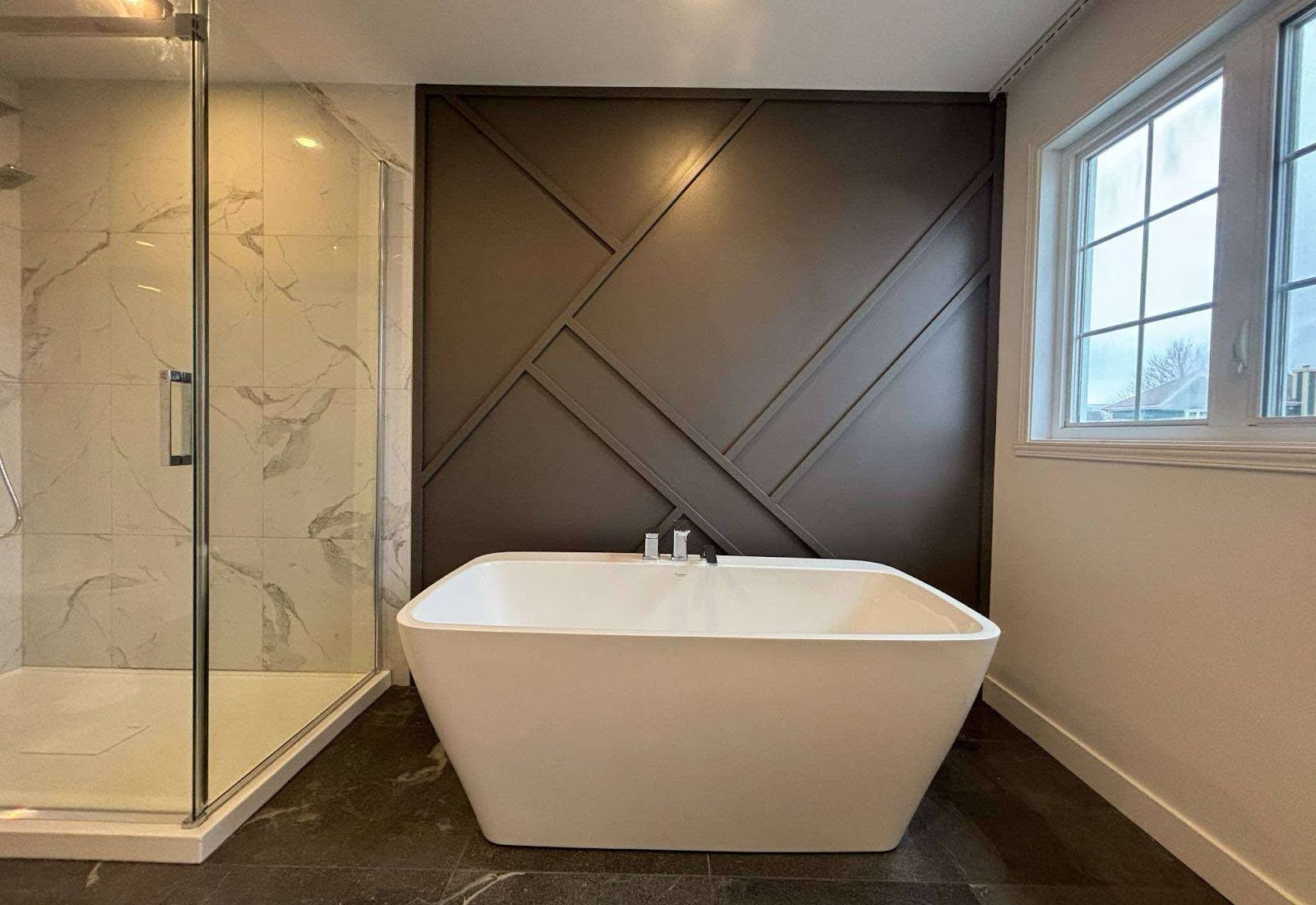 Salle de bain terminée : douche vitrée, bain autoportant, mur d’accent foncé.